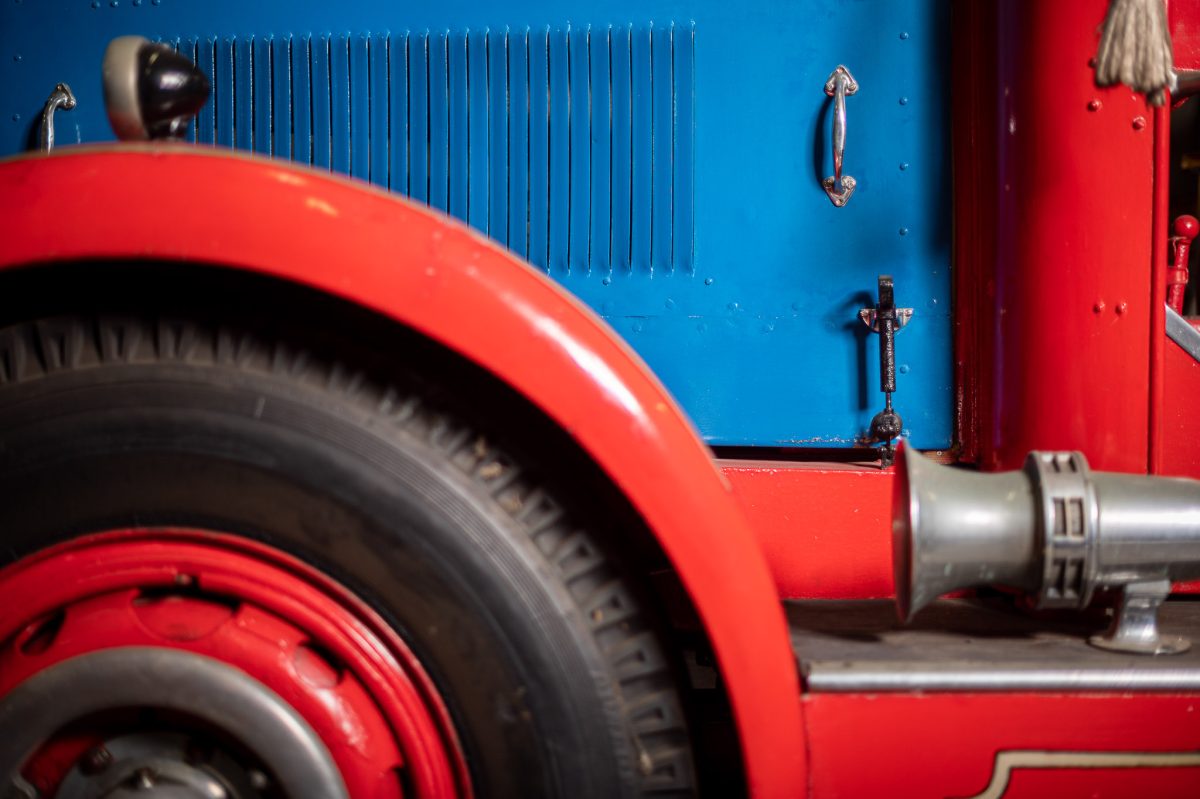 A close up view of an old firetruck. It has a blue engine hood, red tyre hoods and black tyres.