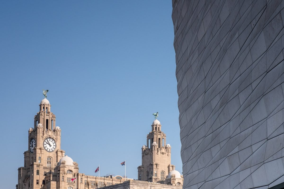 Standing next to the Museum of Liverpool looking across to the top of the Liver Building. There are 3 flags on the Cunard Building next to it. One is the LGBTQ+ Progress Pride flag.