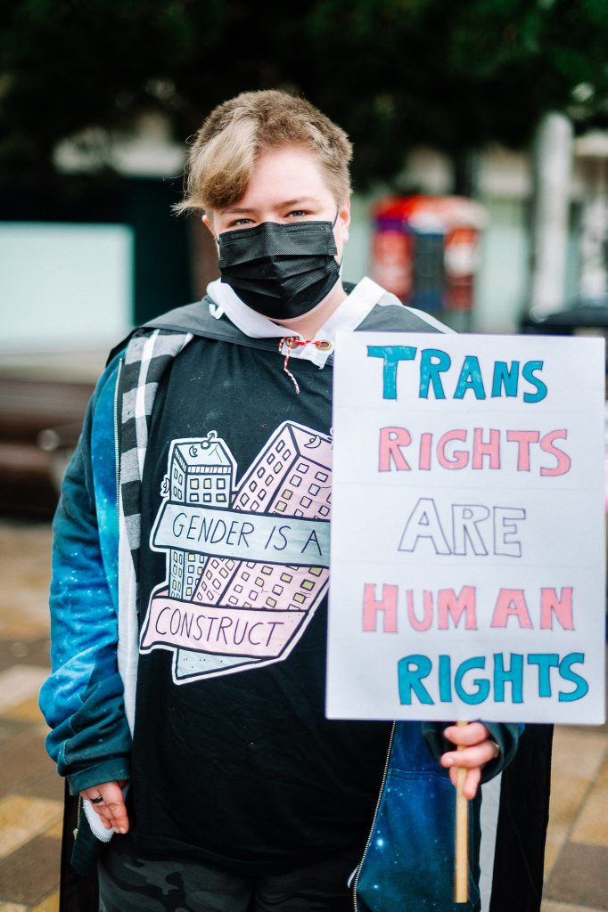A person wearing a face mask holds up a sign saying "Trans rights are human rights."
