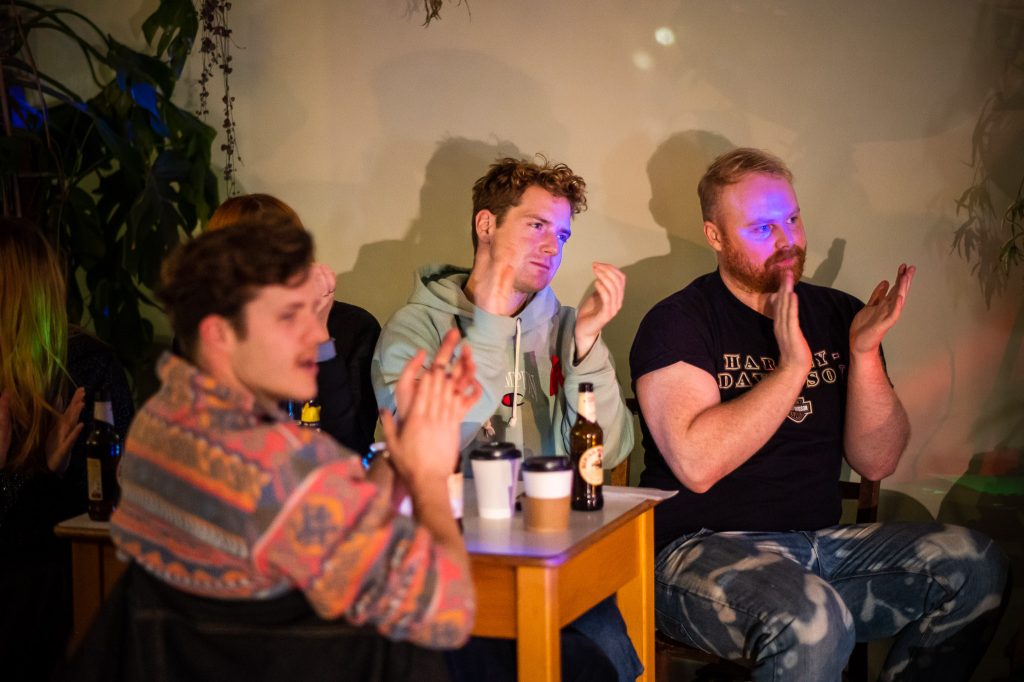 A group of men clap after the singer finishes a set in a cafe.