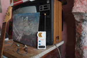 A 1980s style toy walkie talkie sits on a small table. Behind is a painting of a ship being propped up by an old 1970s TV.