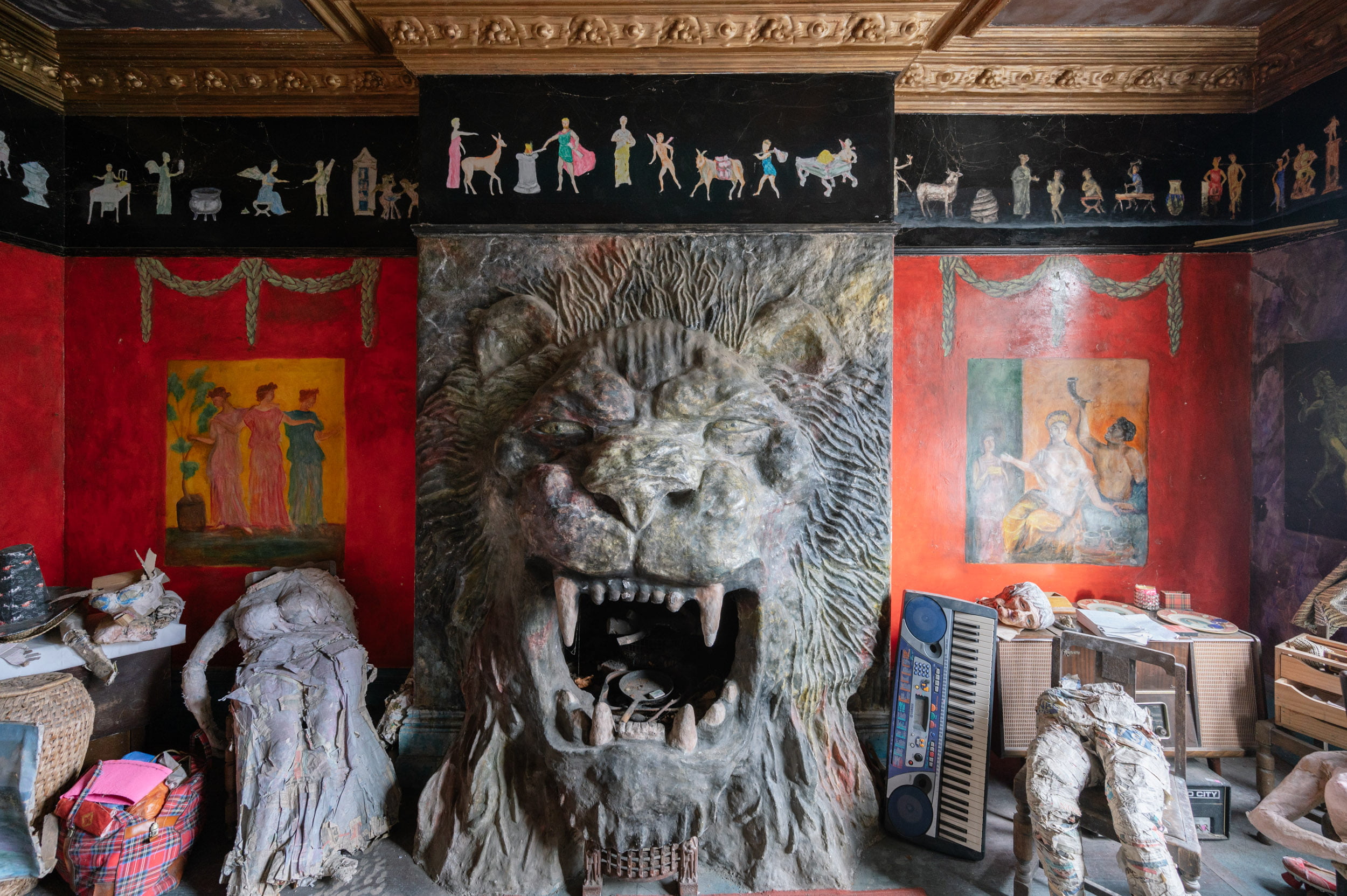 In a red room a large lion made from concrete extends out of what would be a fireplace. Around the room there are all sorts of bits of art.