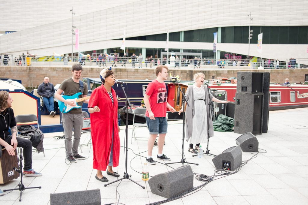 A band performs by the canal outside the Museum of Liverpool as canal barges sail past.
