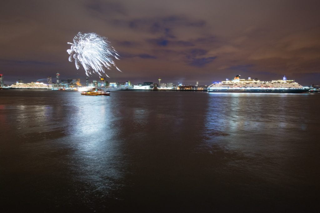 Fireworks light up the sky while 2 Cunard ships sit in the River Mersey.
