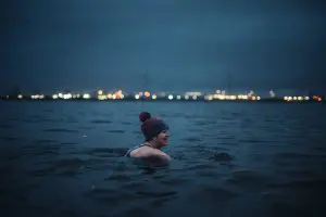 A woman wearing a bobbly hat smiles as she swims in the waters of the River Mersey.