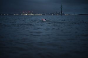 A man swims out towards the Liverpool skyline at dusk.