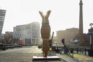 A large art installation made from ropes sits by the Liverpool docks at sunrise.