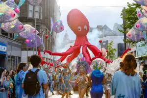 A giant red octopus makes its way down a major street in Liverpool. In front there are Samba dancers.