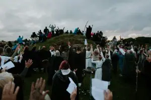 Druids stand on a small mound and raise their hands to the sun on an overcast summer equinox.