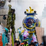A small yellow and blue submarine passes through the city with musicians playing inside.