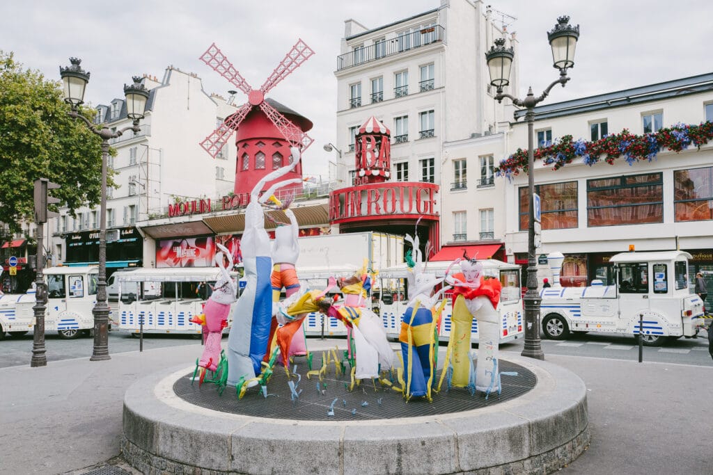 Colourful inflatables are positioned over an air vent outside the Moulin Rouge. They appear to be dancing with their air.