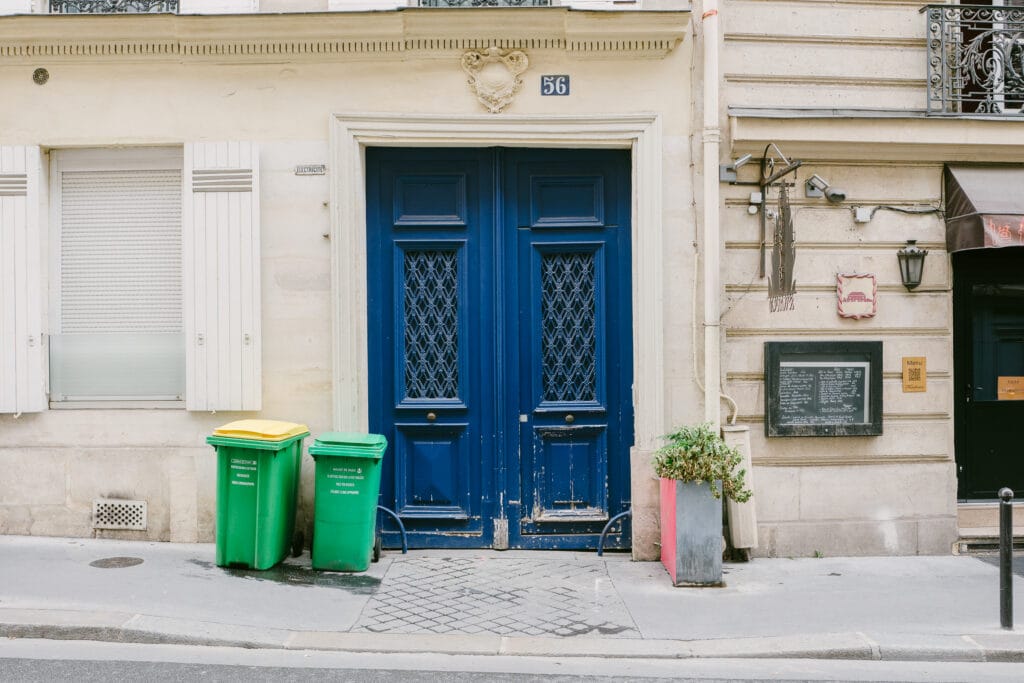 A big blue door in Paris. On the left are green wheelie bins.