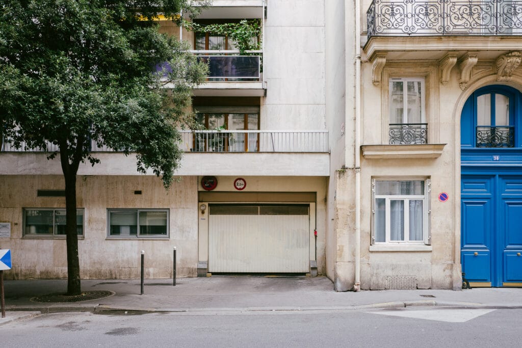 A street in Paris. On the right is a big blue door. In the centre, a garage. On the left is a big tree.