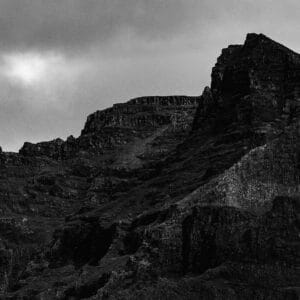 A dramatic black and white image of rugged mountain peaks under a cloudy sky, showcasing sharp and jagged rock formations.