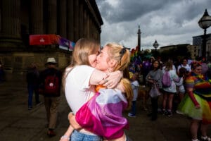 Two lesbian women kiss at Pride outside St Georges Hall. One is wearing the lesbian flag.