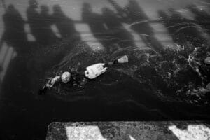 A swimmer reaches the turning point to the finish line. There are silhouettes of supporters cast onto the river by the afternoon sun.