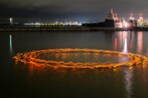 A group of swimmers wear orange lights and swim in a circle. It creates an orange circle on the top of the lake at night.