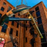A large anchor is being lifted by a crane in front of the Maritime Museum in Liverpool.