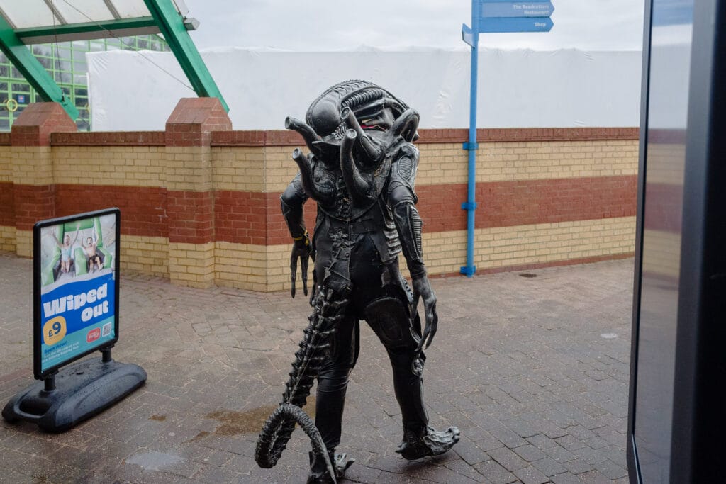 A person in an alien costume walks away from the camera at an event.