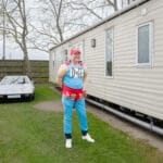A man dressed in a Duff beer costume stands in front of a mobile home.
