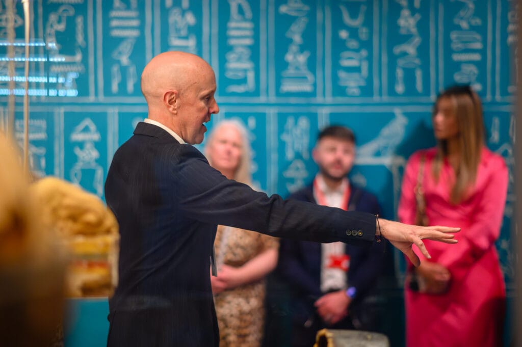 A man in a suit is giving a presentation at the World Museum Liverpool. There are other people in the background.