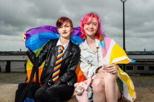 Two people at Liverpool Pride, holding Pride flags and smiling.