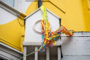 A close-up shot of a white building with colorful ribbons hanging from it, likely for a Pride event.