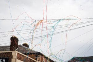 Confetti and streamers float in the air against a cloudy sky, above rooftops.