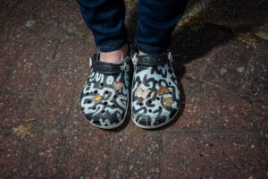 Close-up of a person's feet in decorated Crocs shoes on a brick surface.