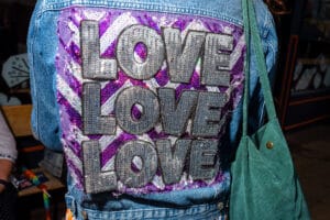 Person wearing a denim jacket with the word 'LOVE' in large, sequined letters on the back, at Wirral Pride.