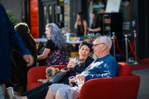 People enjoying Wirral Pride 2025 in New Brighton, sitting on a red sofa. A small dog is also present.