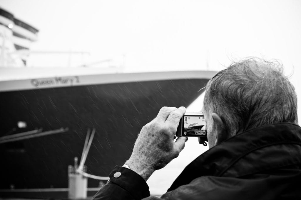 An older man takes a photograph of the Queen Mary 2 cruise ship in Liverpool, England.