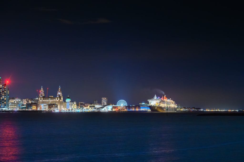 A night view of Liverpool's skyline with the cruise liner Queen Mary 2 (QM2) sailing on the Mersey River.