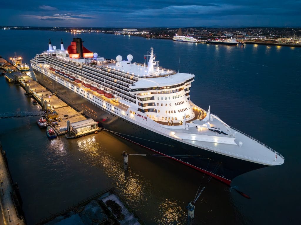 Aerial view of the Cunard cruise liner Queen Mary 2 docked in Liverpool, illuminated at dusk.